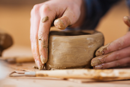 Closeup of earthen jar making by hands of young woman potter on wooden table in workshop