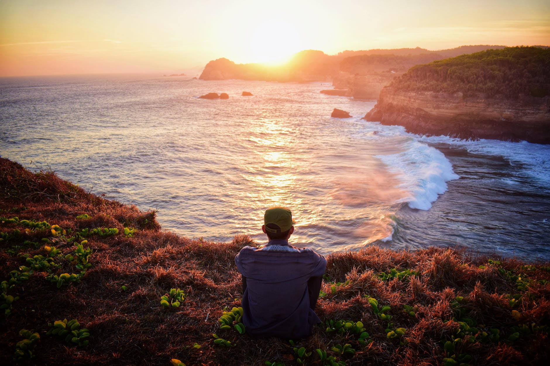 man sitting on grass by the cliff