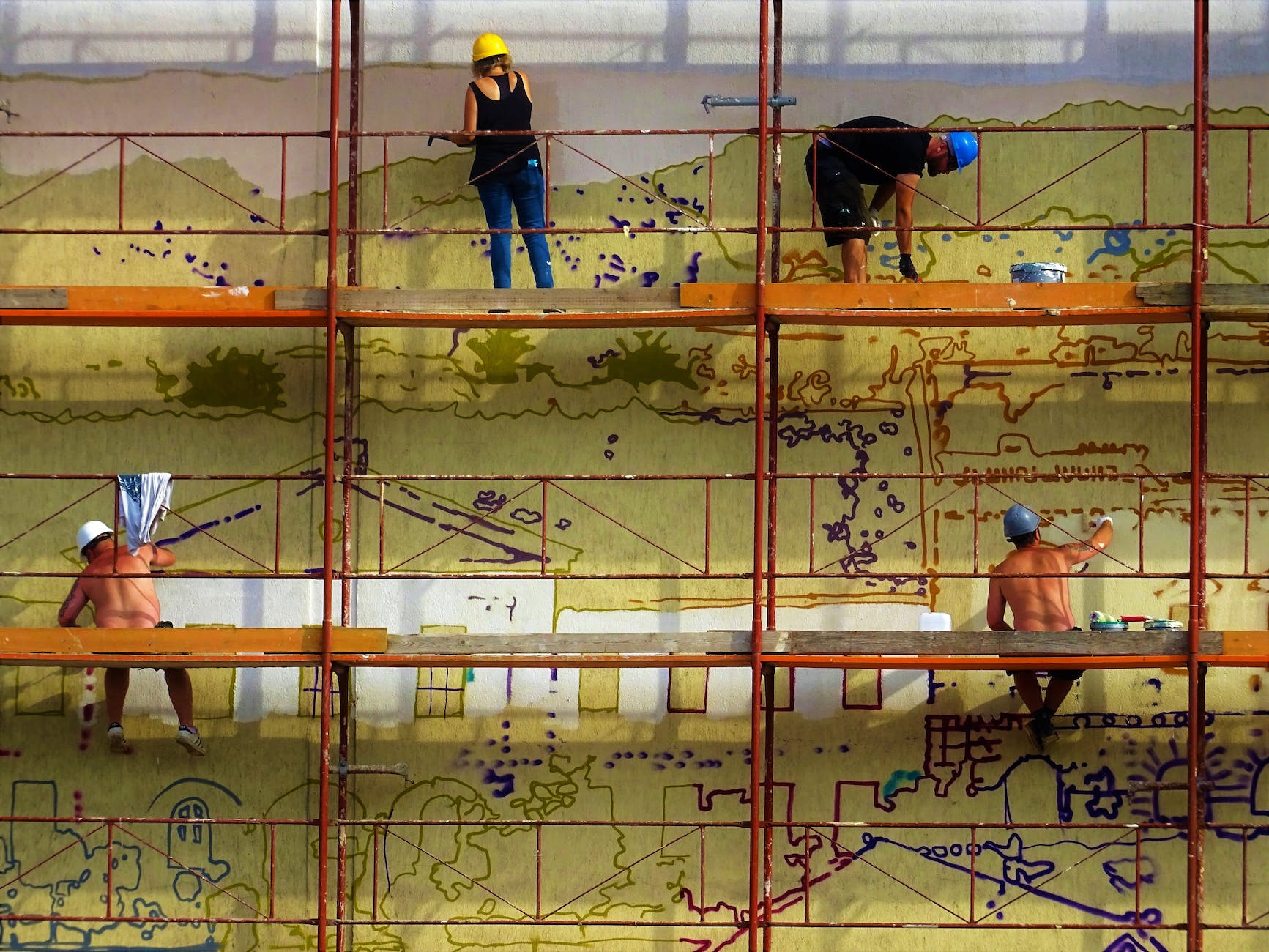 four people painting wall on scaffolding